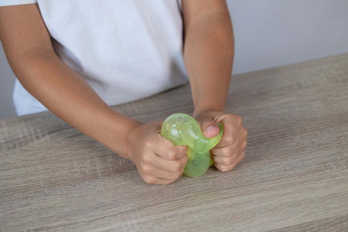 Child's hands squeezing a translucent green stress toy in soft daylight